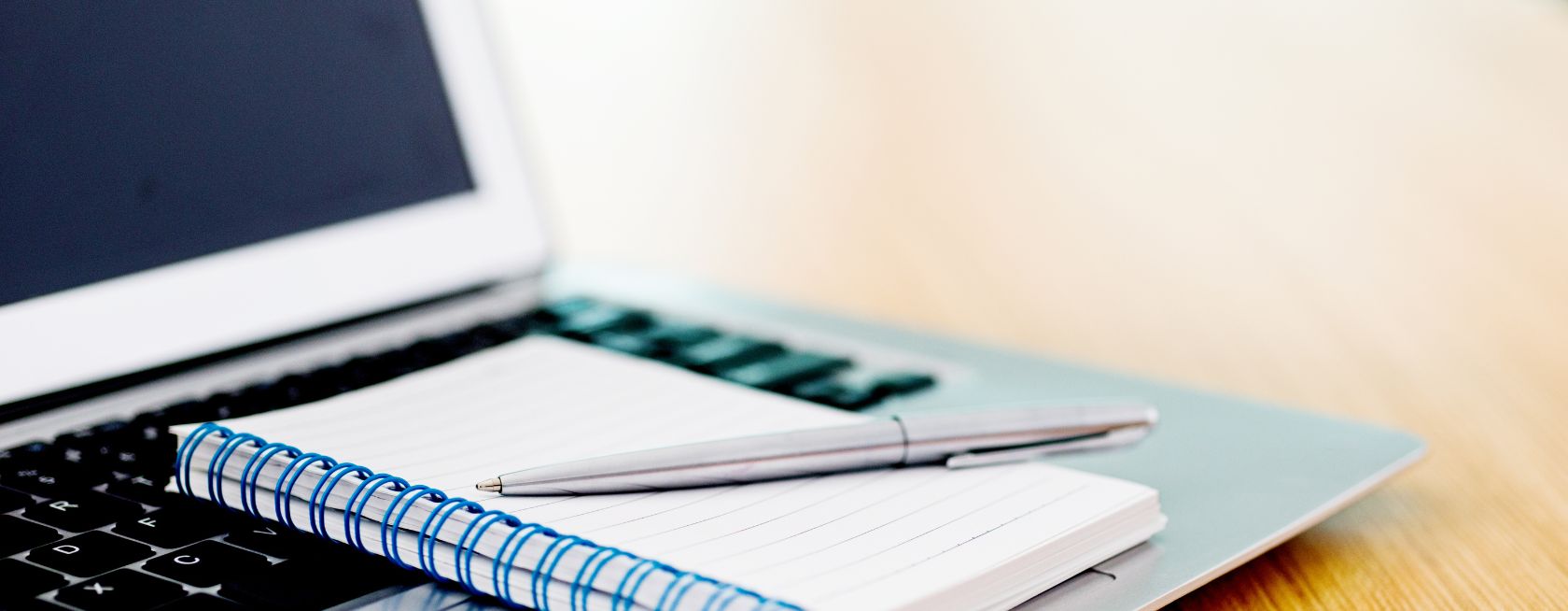 Laptop with pen and spiral notebook on desk