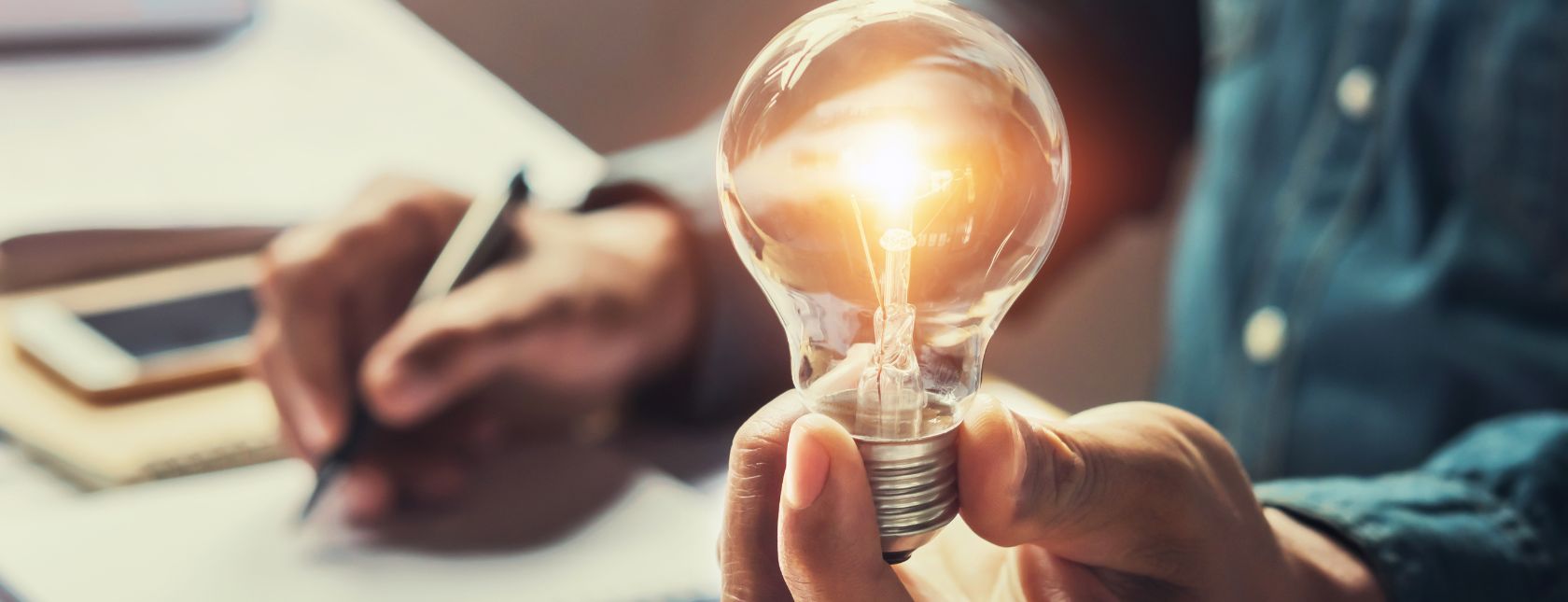 Medarbejder sidder med en pære i den ene hånd og skriver noter med den anden